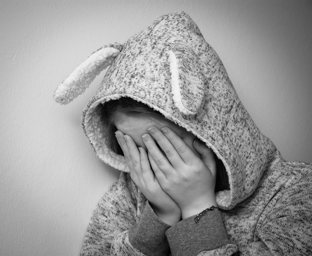 black and white image of child wearing a hooded jumper with bunny ears attached with their hands covering their face